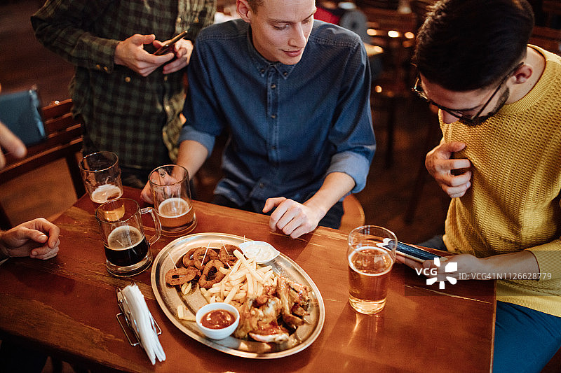 酒吧里的人一边喝啤酒一边看智能手机图片素材