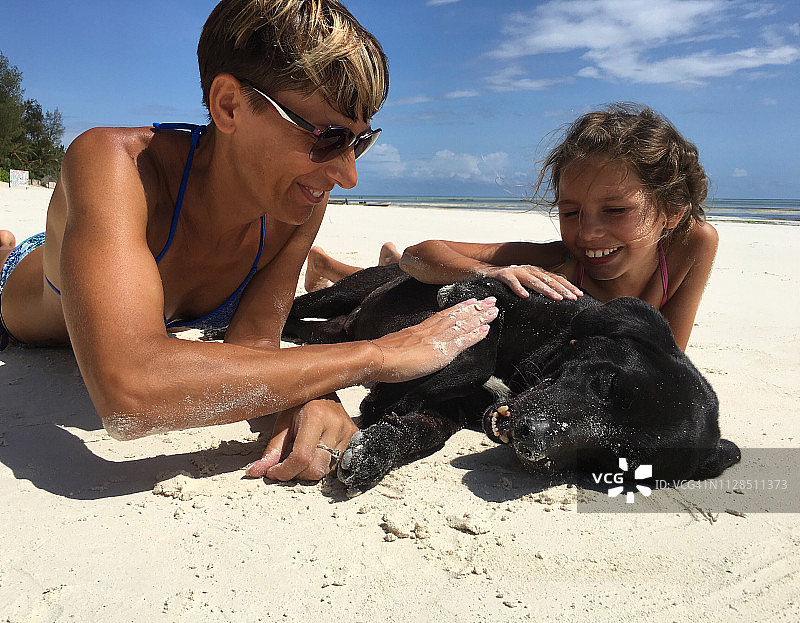 母亲和女儿和他们的狗在沙滩上享受图片素材