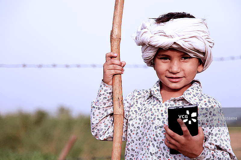 可爱的小男孩站在绿色的田野附近拿着手机图片素材