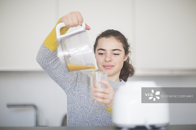 微笑的女人往厨房里的杯子里倒鲜榨橙汁的肖像图片素材