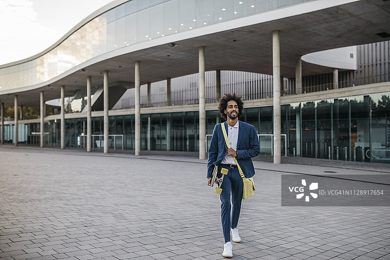 西班牙巴塞罗那，年轻的商人手拿滑板离开办公楼的城市图片素材