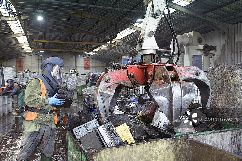 在汽车电池回收厂，穿着防护服的工人将汽车电池装入抓取箱图片素材