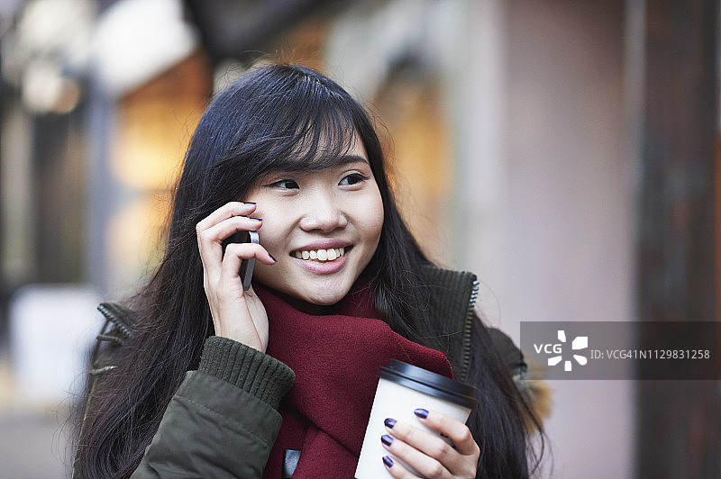 一名年轻女子正用智能手机走在购物街上图片素材