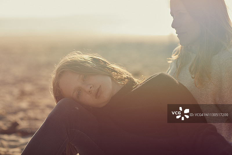 一个年轻的女儿和她的妈妈在柔和的阳光下的海滩上的肖像图片素材
