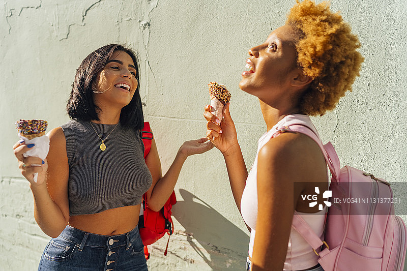 两个快乐的女性朋友拿着甜筒冰淇淋站在墙上图片素材
