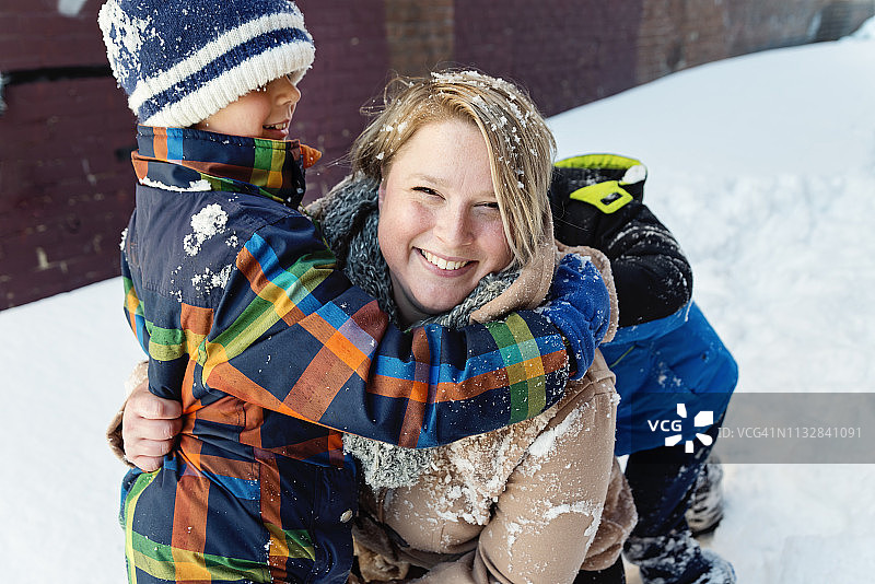 身体积极的母亲与她的两个儿子在雪户外玩。图片素材