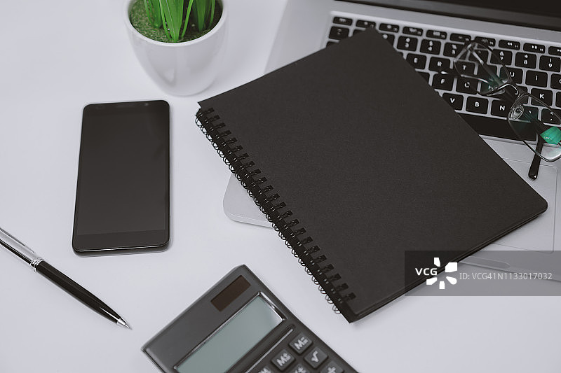 黑色螺旋笔记本，笔记本电脑和移动电话在办公桌上图片素材