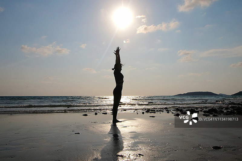 日落时分，一个年轻女子在沙滩上练习瑜伽图片素材