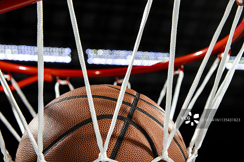 看着一个篮球从球网中落下，背景是球场的灯光图片素材