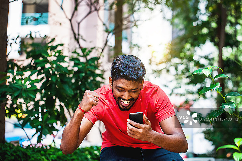 年轻的马来西亚印度男子用智能手机庆祝成功图片素材