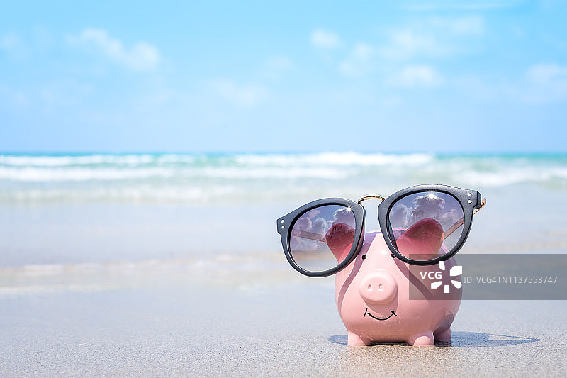 存钱旅行的概念，粉色小猪储蓄罐戴着太阳镜在海滩上图片素材