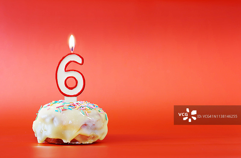 六年的生日。纸杯蛋糕，上面有燃烧着的白色蜡烛，形状是数字6。鲜艳的红色背景与复制空间图片素材