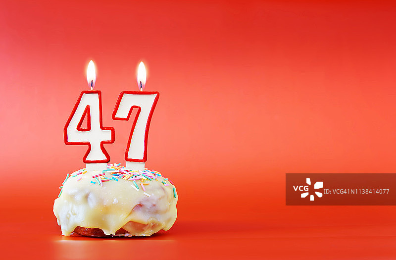四十七岁生日。纸杯蛋糕，上面有燃烧着的白色蜡烛，数字是47。鲜艳的红色背景与复制空间图片素材