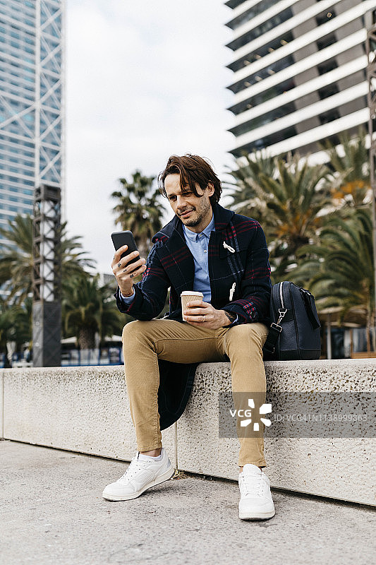 西班牙，巴塞罗那，一个男人坐在城市里拿着外卖咖啡和手机图片素材