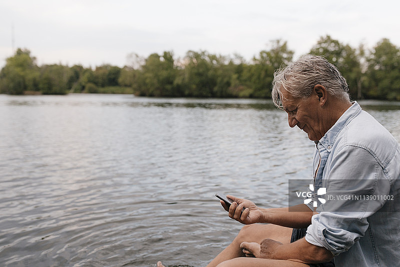 一个老人坐在湖边玩手机图片素材