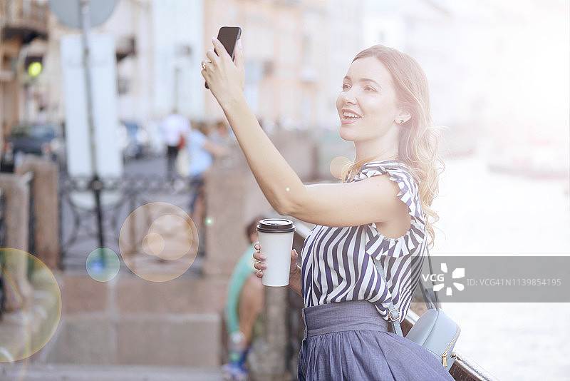 年轻女子在圣彼得堡散步(电话、咖啡、自拍)图片素材