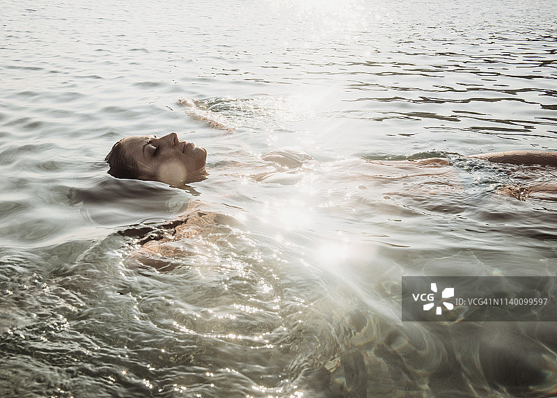 年轻女子漂浮在阳光灿烂的海面上图片素材