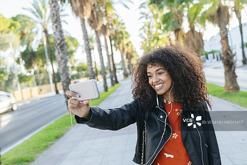 微笑的年轻女子用智能手机自拍的照片图片素材