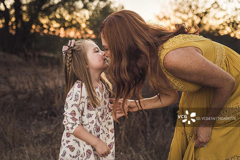 在加利福尼亚的田野里，一名妇女弯下腰亲吻她的小女儿图片素材