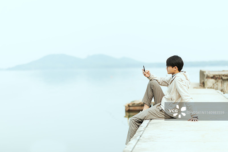 一个年轻人坐在码头上用手机图片素材
