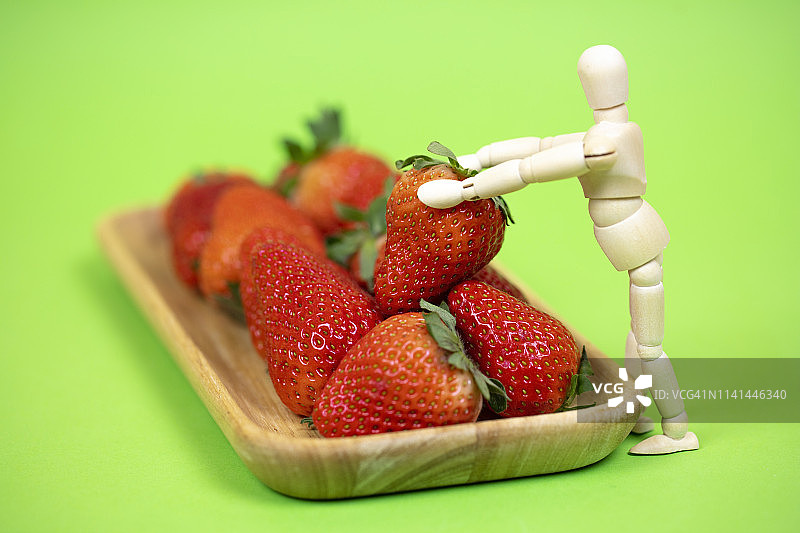 拿着水果的木制人体模型。草莓图片素材