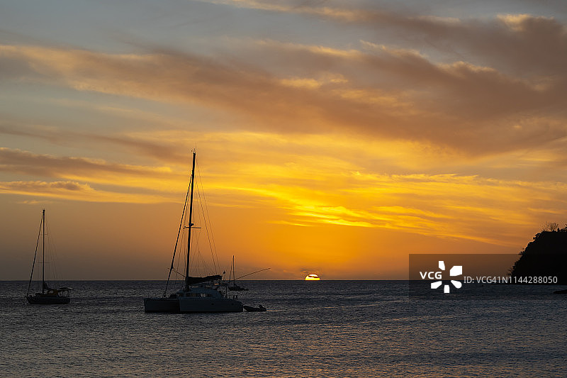 在努美阿的柠檬海滩上，游艇的剪影映出夕阳的余晖图片素材