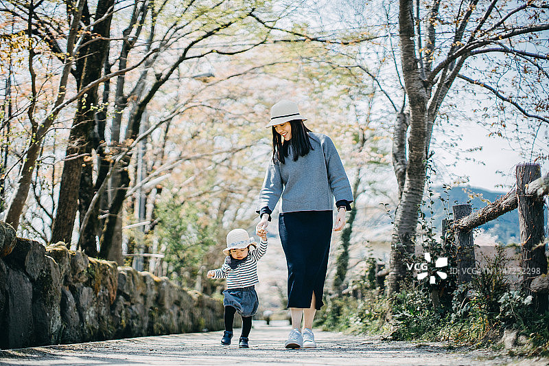 慈爱的年轻亚洲母亲牵着可爱的小女儿在自然的小路上散步，享受亲密的家庭时光图片素材