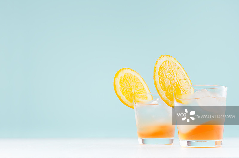 鲜冷酒精条纹饮料与橙酒，切片水果，冰在优雅的绿色背景和白色木板。图片素材