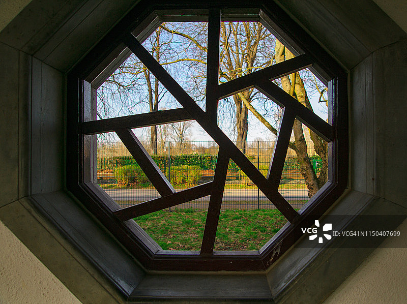 透过中式八角形木雕窗框，可以看到公园的景观图片素材