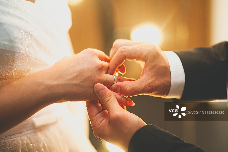 新郎把戒指戴在新娘的手上。婚礼当天新婚夫妇的手，特写。结婚期间交换戒指。图片素材