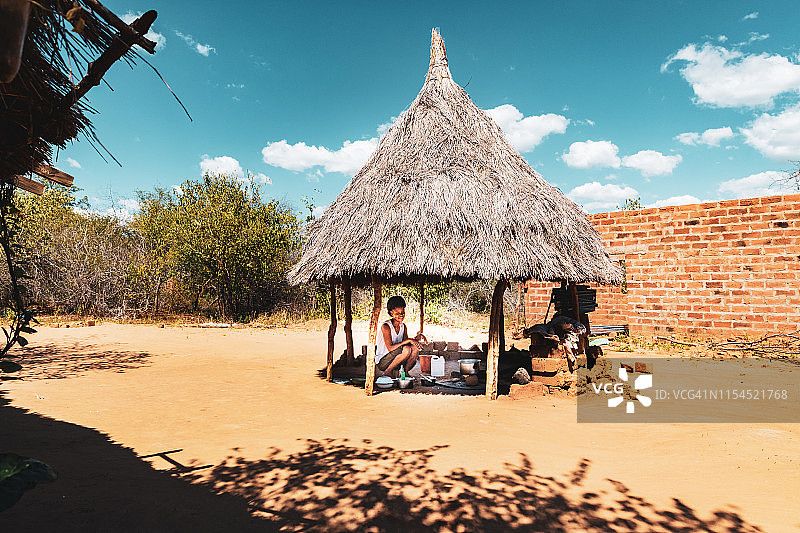 一个年轻的女人在非洲村庄的小屋下烹饪玉米迷宫图片素材