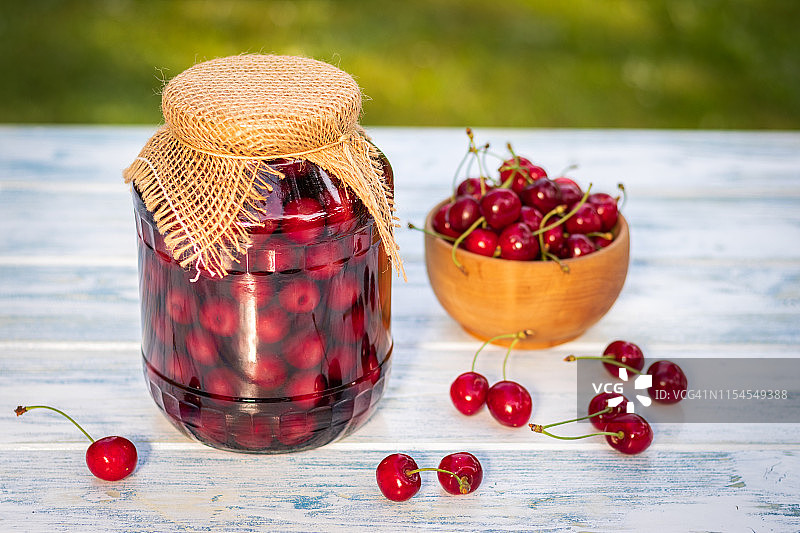 罐装樱桃水果和新鲜收获的樱桃在碗里放在木桌上。图片素材