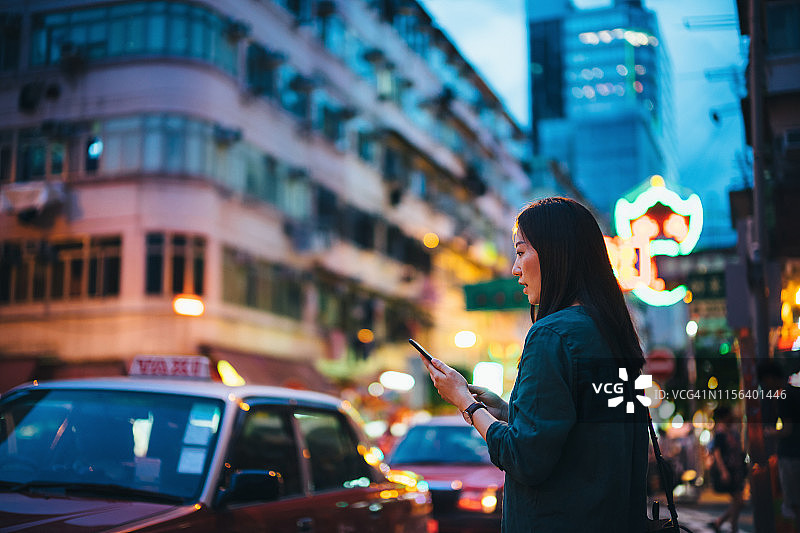 一名年轻女子一边走在路上一边用手机，背景是当地的街景和繁忙的交通图片素材