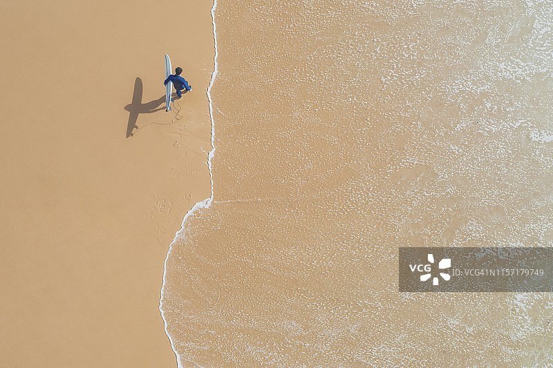 葡萄牙，阿尔加维，萨格雷斯，普拉亚达马雷塔，男子在海滩上携带冲浪板鸟瞰图图片素材