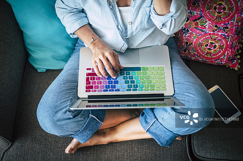 一个女人在家里的沙发上使用笔记本电脑和五颜六色的键盘图片素材