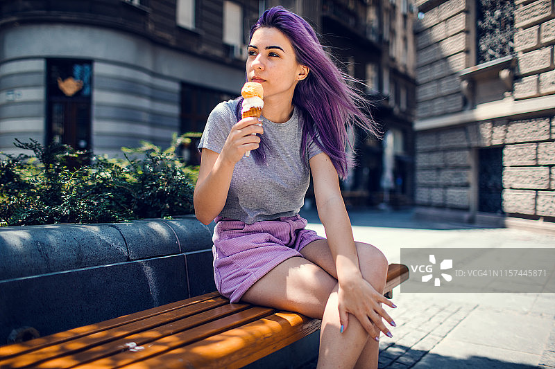 吃冰淇淋的紫色头发的年轻女人图片素材
