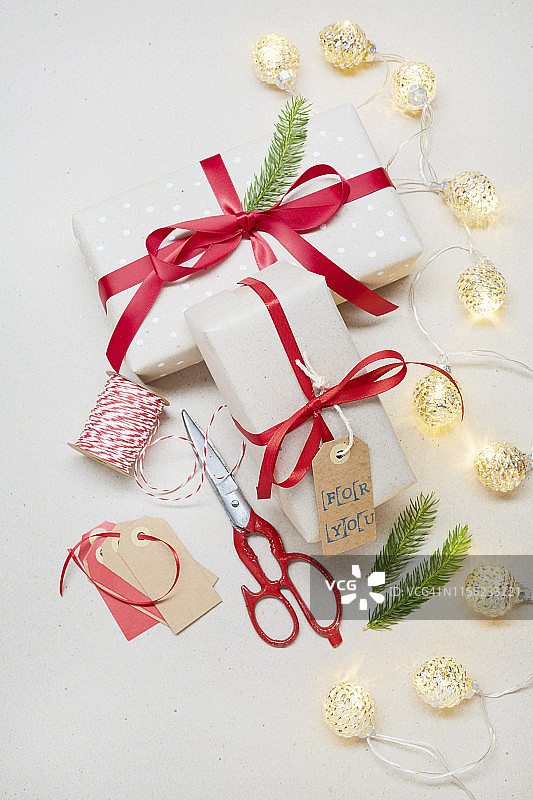 上图是在灰色背景上用“为你”的礼物标签包装圣诞礼物，红色剪刀和圣诞灯图片素材