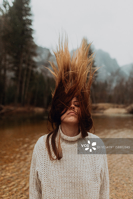 美国加利福尼亚州约塞米蒂村，一位年轻女子在河岸上摇晃着棕色的长发图片素材