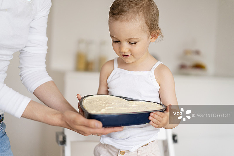 小女孩和妈妈在厨房里一起拿着一个烤盘和蛋糕糊图片素材