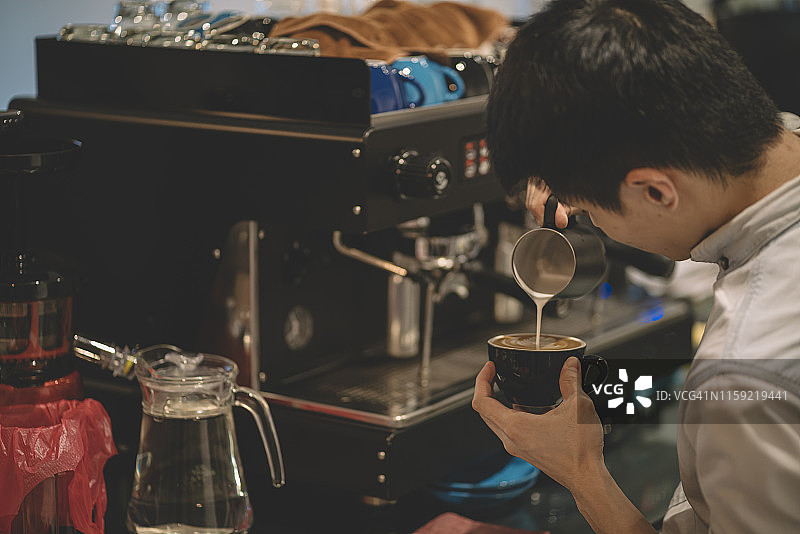 一位亚洲华人咖啡师店主正在为他的顾客准备拿铁咖啡图片素材