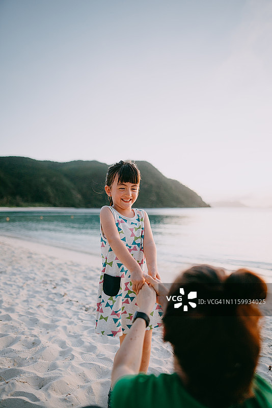 日落时分，日本冲绳县海滩上，快乐的混合种族学龄前女孩牵着母亲的手图片素材
