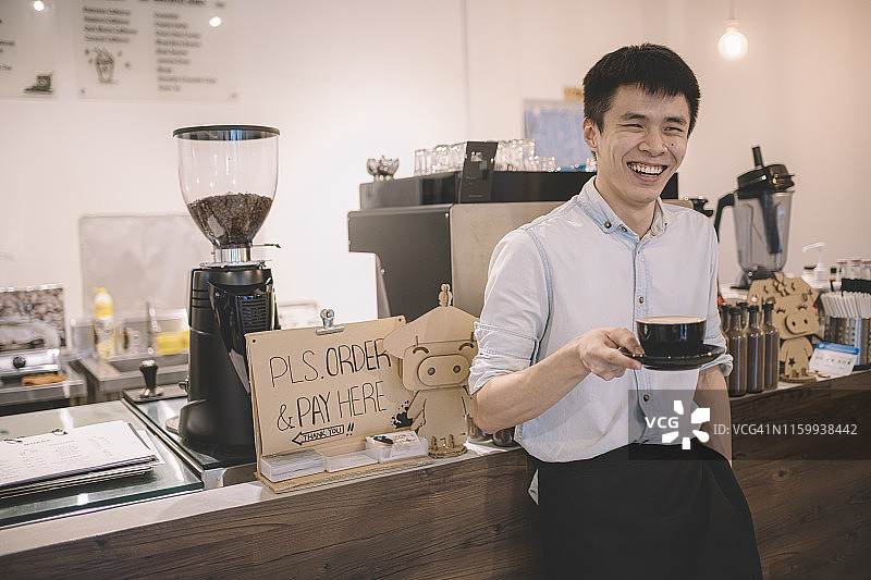 一位亚裔华人咖啡店老板站在他的咖啡店柜台前微笑着图片素材