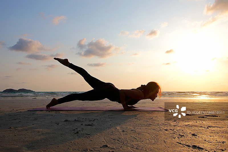 日落时分，一个年轻女子在沙滩上练习瑜伽图片素材