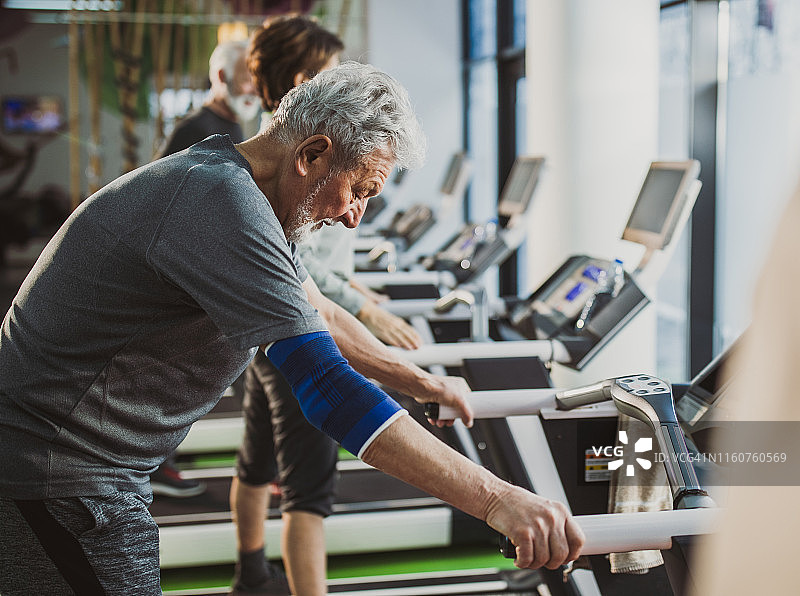 疲惫的老人在健身房里的跑步机上锻炼休息。图片素材