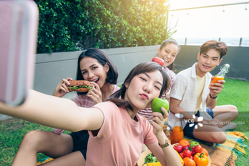 一群快乐的亚洲朋友用手机自拍，享受在户外公园野餐，健康的食物和生活理念图片素材