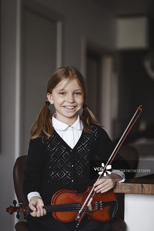 一个在家里拿着小提琴的微笑女孩的肖像图片素材