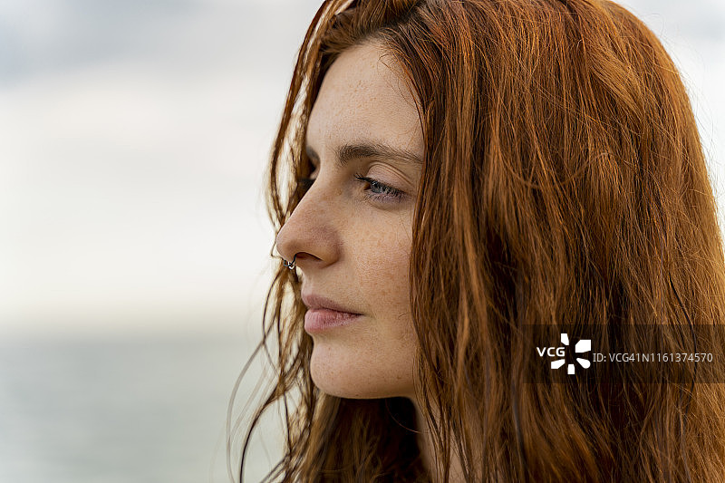 肖像沉思红发年轻女子穿鼻在大海在日落图片素材