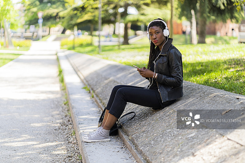 一个女人在城市公园里拿着手机和耳机休息图片素材