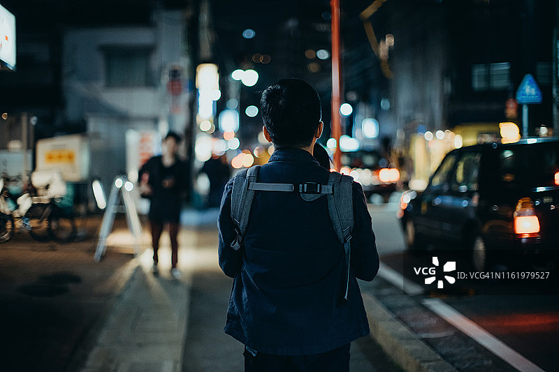 年轻的亚洲父亲背着小女儿在夜晚穿过城市的街道，与繁忙的交通灯光景观图片素材