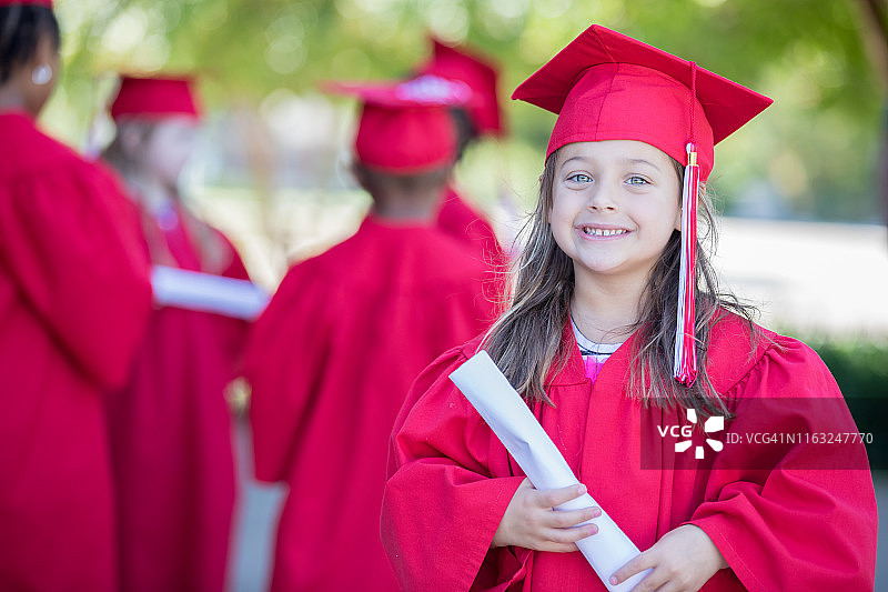 可爱的学龄前小女孩拿着毕业证书，戴着毕业帽，穿着毕业服图片素材